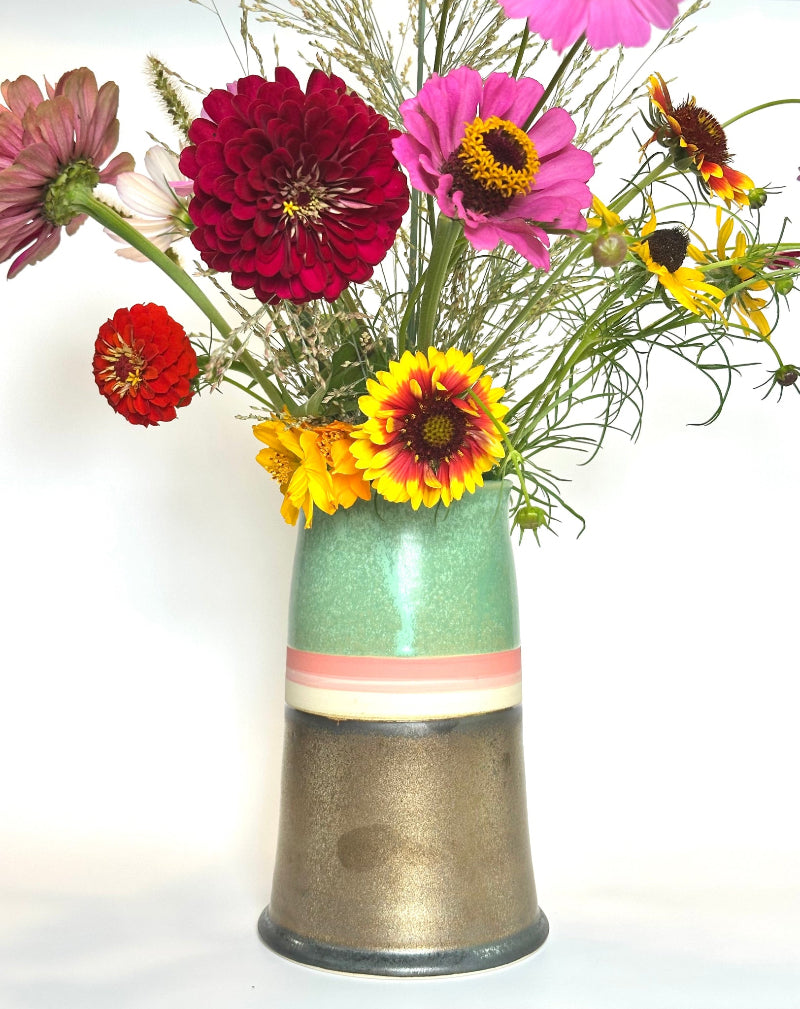 A ceramic vase filled with a colorful assortment of wildflowers, including red, pink, yellow, and orange blossoms, set against a plain white background.